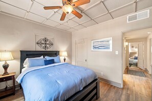 Ein Schlafzimmer mit einem Bett, zwei Nachttischlampen, einem Deckenventilator, einer Wanddekoration und einer Tür zu einem anderen Raum.