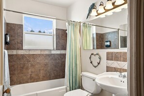 Ein Badezimmer mit Badewanne, Toilette und Waschbecken. Über der Badewanne befindet sich ein Fenster und eine Duschvorhang.