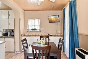 Eine Küche mit Esstisch, Stühlen, einem an der Wand befestigten Fernseher und einem Fenster mit Vorhängen.