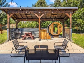 Eine Außenpatio mit einer Pergola, einem Grill, Holzfässern und einer fassförmigen Holzkonstruktion.