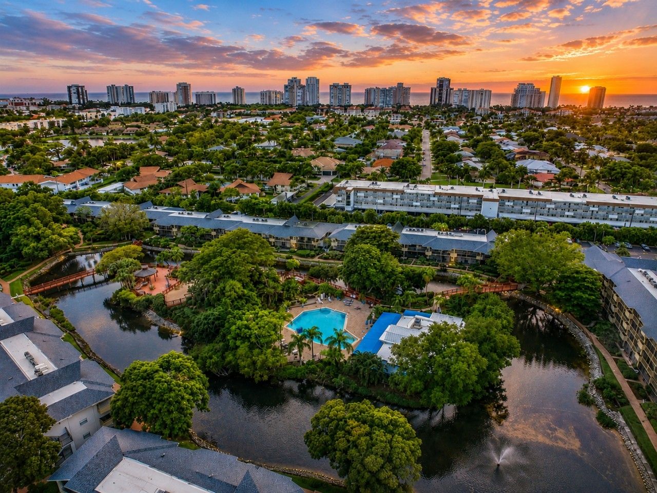 A residential area with a central swimming pool surrounded by greenery and a body of water.