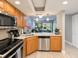 A modern kitchen with wooden cabinets, stainless steel appliances, and a dishwasher. - Park Shore Resort, Top Floor BLDG G #341-Corner condo (Park Shore Resort)