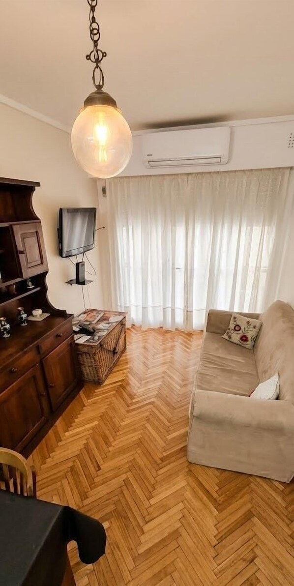 A living room with a herringbone floor, a sofa, a television, and a hanging light fixture. - Central Recoleta Apartment for 4 Guests (Recoleta)