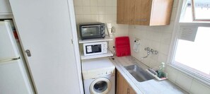 A compact kitchen with a washing machine, a microwave, a toaster, and a red dish rack. - Central Recoleta Apartment for 4 Guests (Recoleta)
