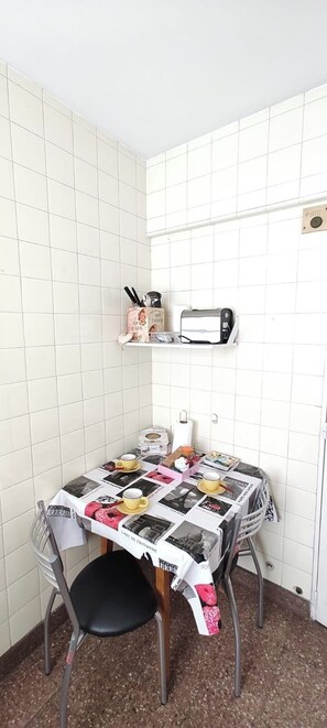 A small kitchen with a tiled backsplash, a microwave, a toaster, and a table with a newspaper-covered tablecloth. - Central Recoleta Apartment for 4 Guests (Recoleta)