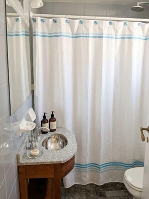 A bathroom with a shower curtain, a sink with a mirror, and toiletries. - Central Recoleta Apartment for 4 Guests (Recoleta)