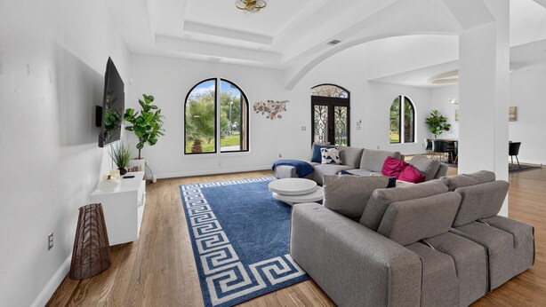 Ein geräumiges Wohnzimmer mit einem grauen Sofa, einem blau gemusterten Teppich und großen Bogenfenstern.