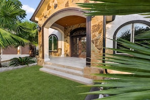 Une maison avec une façade en pierre, un porche à l’avant avec des marches et une grande porte d’entrée en arc de cercle.