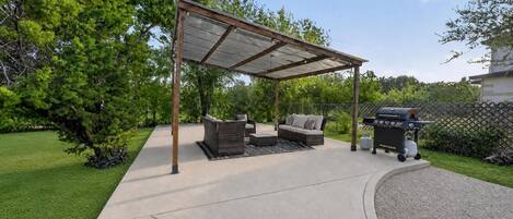A covered patio area with outdoor furniture and a barbecue grill.