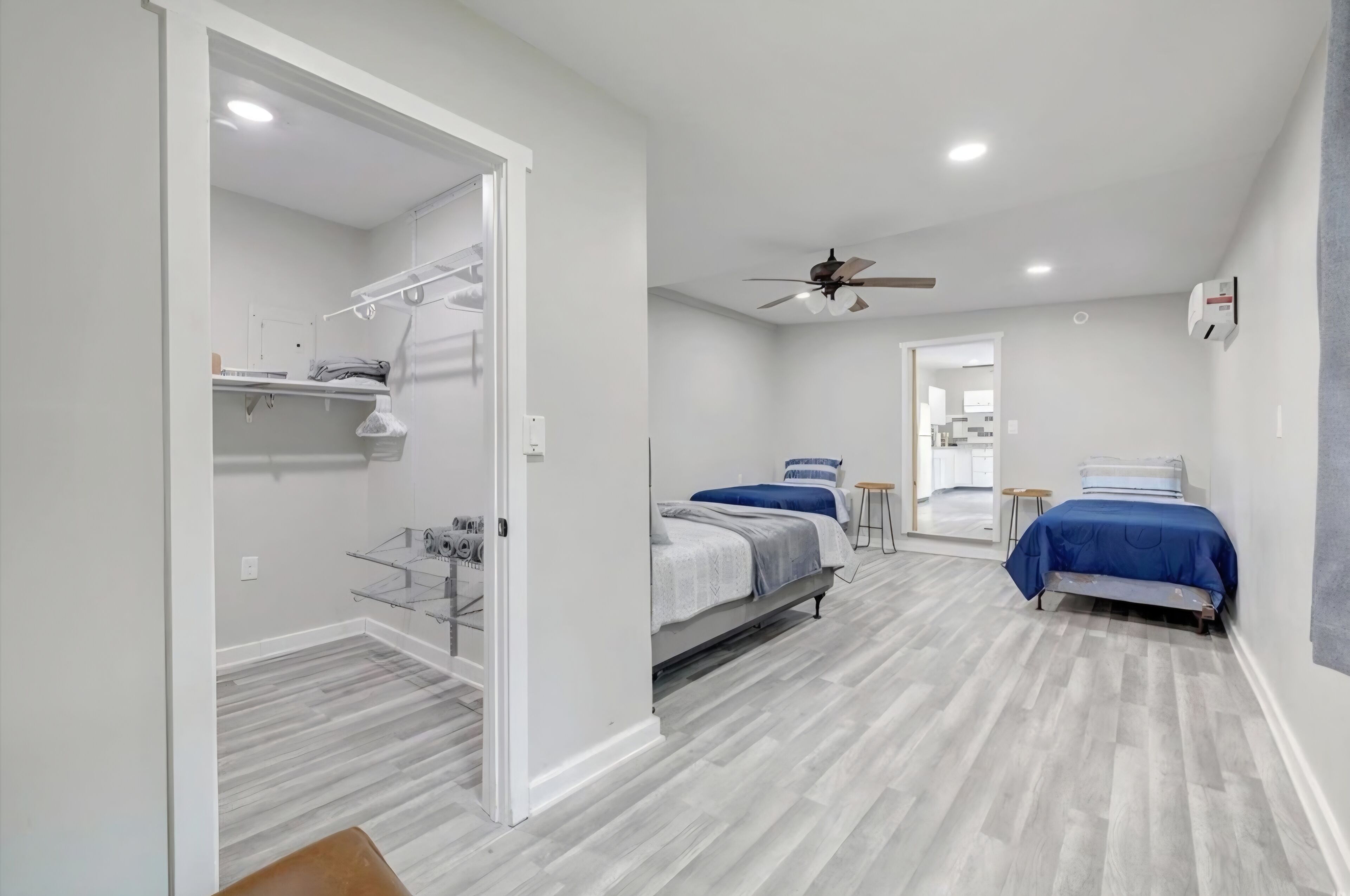Une chambre moderne avec deux lits, un ventilateur de plafond et un dressing avec des étagères.