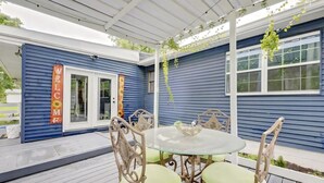 A covered patio area with a round glass table and four chairs, a white pergola overhead, and a blue building with a 'WELCOME' sign. - Apartamento en Bloomington (Bloomington)