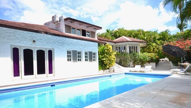 Piscina com um edifício branco adjacente, com telhado vermelho e varanda.