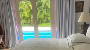 Quarto de hotel com cama, abajur e vista para uma piscina através de uma porta de vidro.
