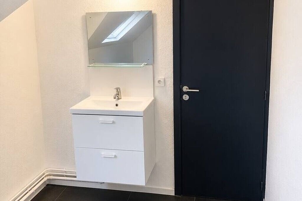 A bathroom with a white sink, a mirror, and a black door.