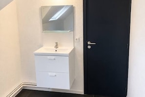 Une salle de bain avec un lavabo blanc, un miroir et une porte noire.