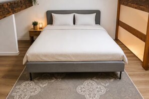 A bed with a grey headboard, white bedding, and a patterned rug. - Bright Duplex Near Grand Place • Self Check-in (Brussels)