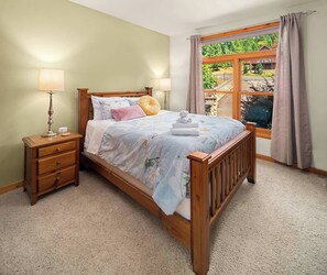 A bedroom with a wooden bed, two bedside tables, a window with curtains, and a view of greenery outside. - Private Mountain Chalet | Timberline | Mt. Rainier (Packwood)