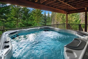 Un bain à remous doté d’une terrasse en bois et d’une rambarde en métal, entouré d’une végétation luxuriante.