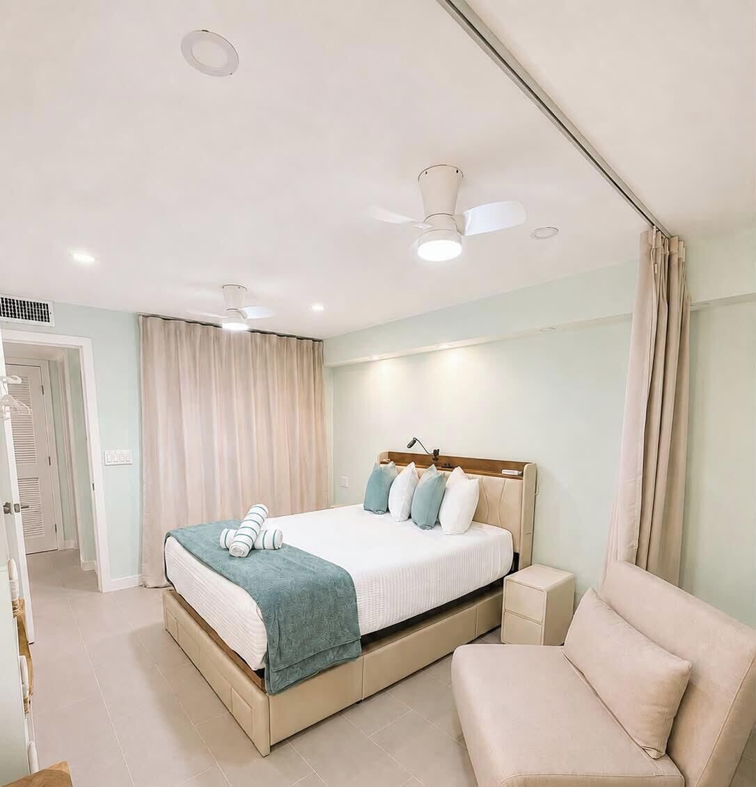 A hotel room with a bed, a chair, a ceiling fan, and a door.