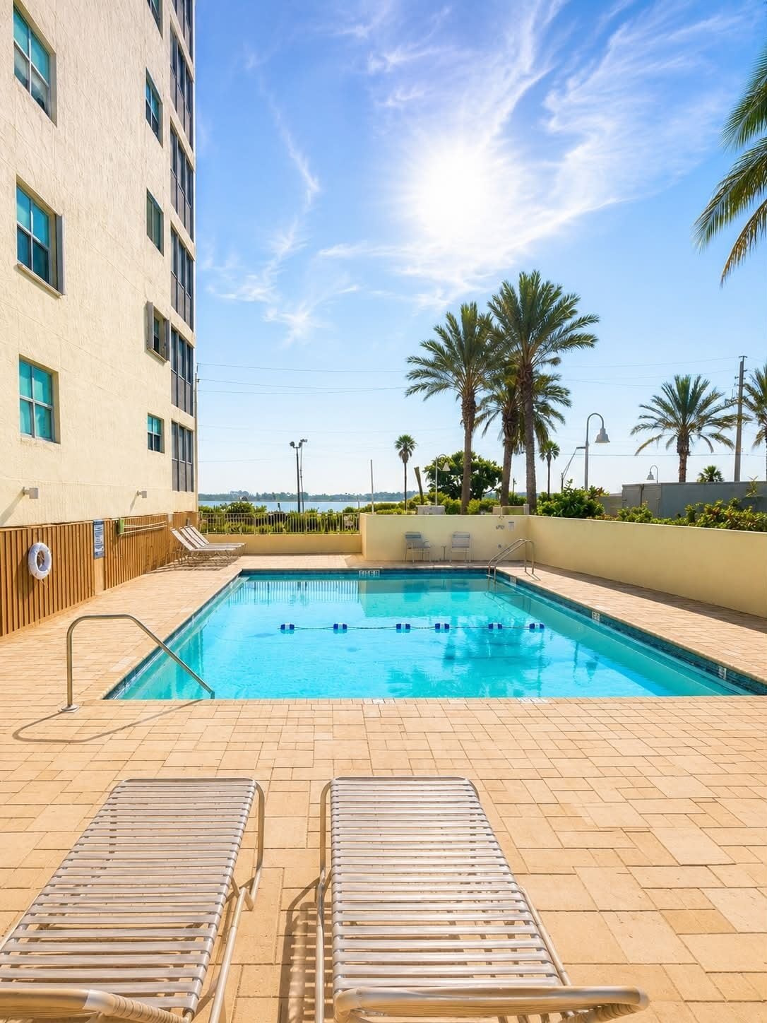Une piscine avec des chaises longues, des palmiers et un bâtiment en arrière-plan.
