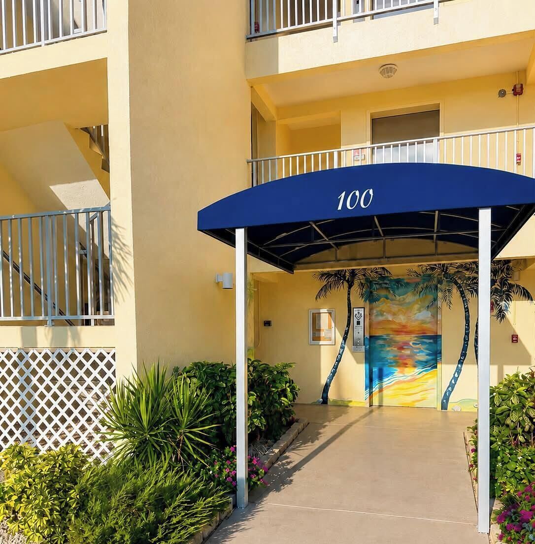 A hotel entrance with a covered walkway, a number '100' sign, a palm tree mural, and a staircase to the left.