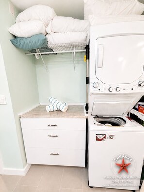 A laundry area with a washing machine, a drying rack, and a storage cabinet.