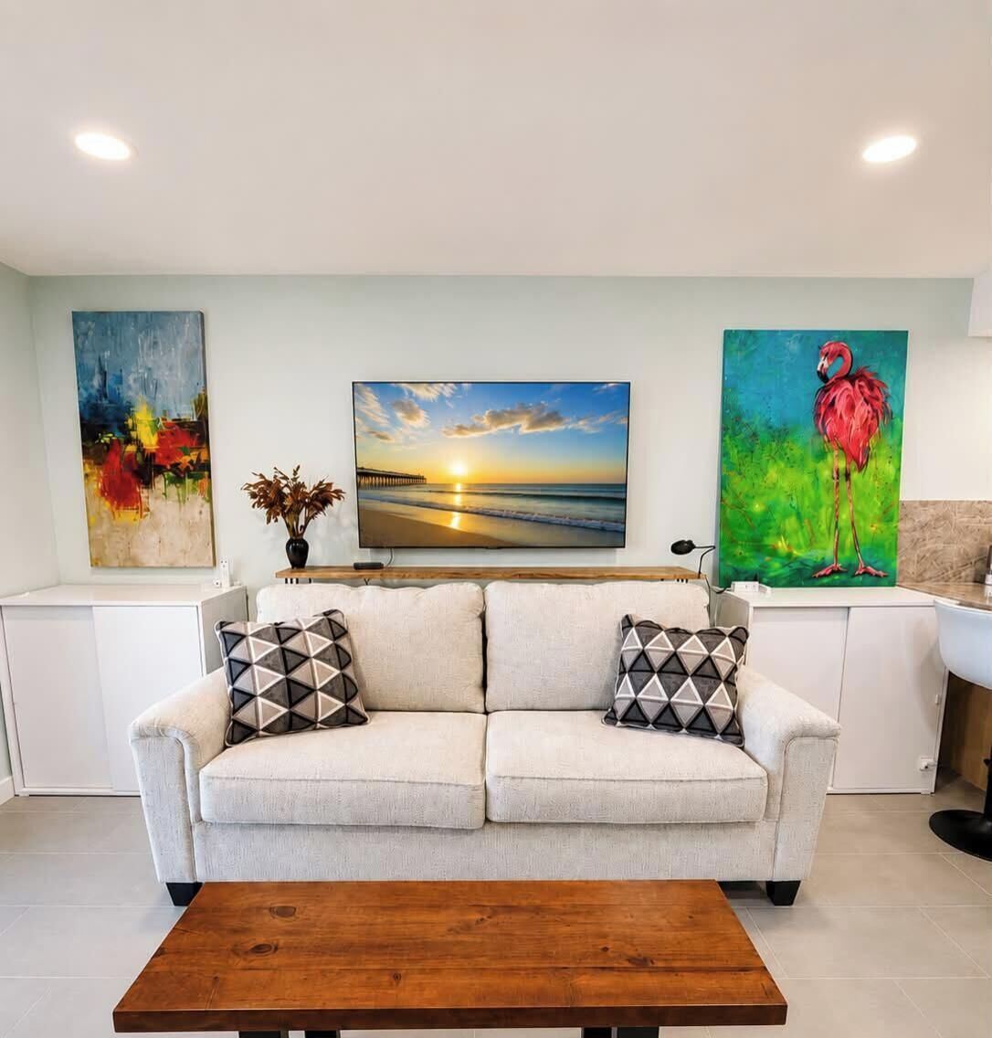 A living room with a sofa, a coffee table, and three paintings on the wall.