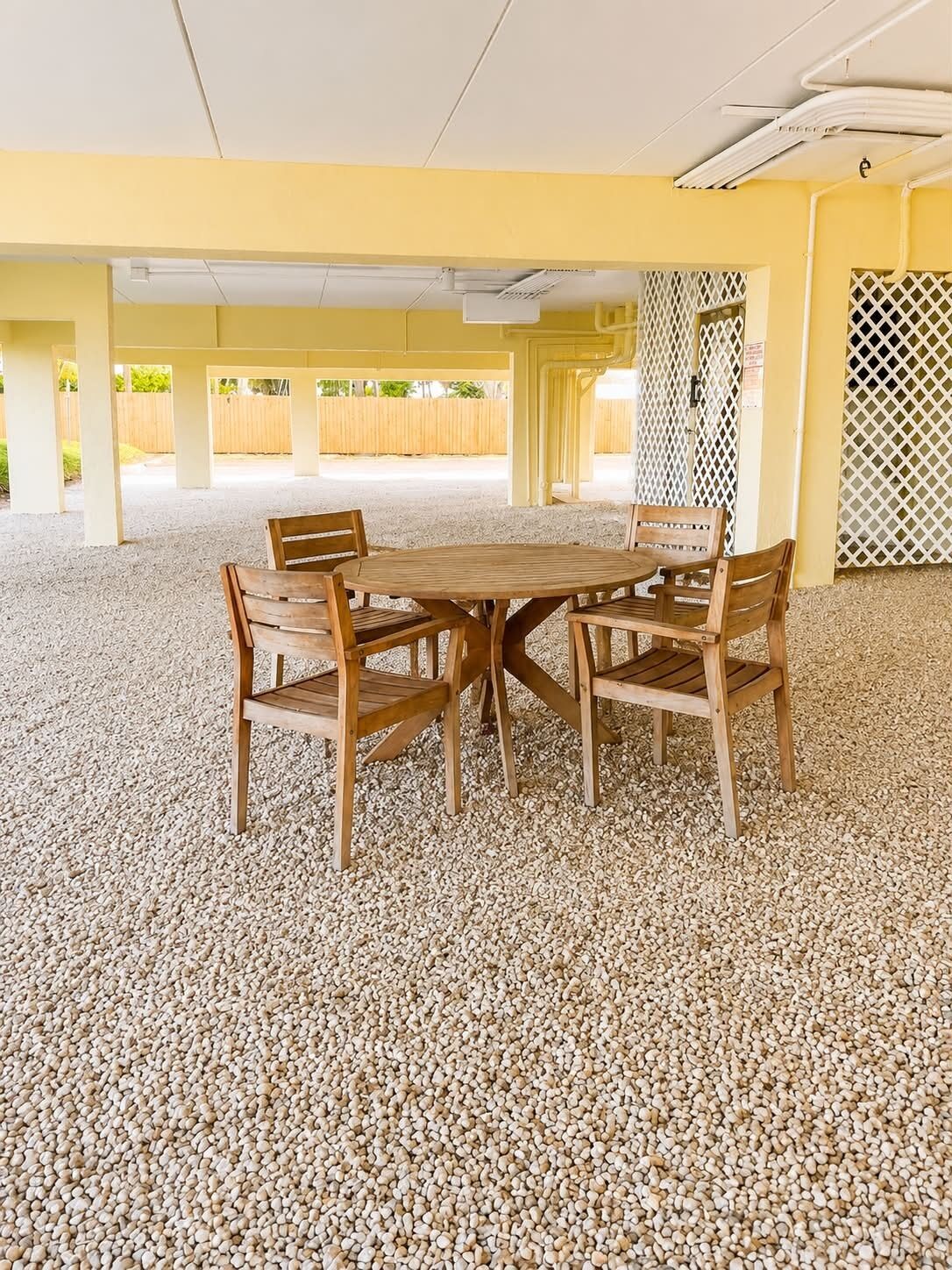 Un área de estar al aire libre con techo, mesa y sillas de madera, rodeada de grava.
