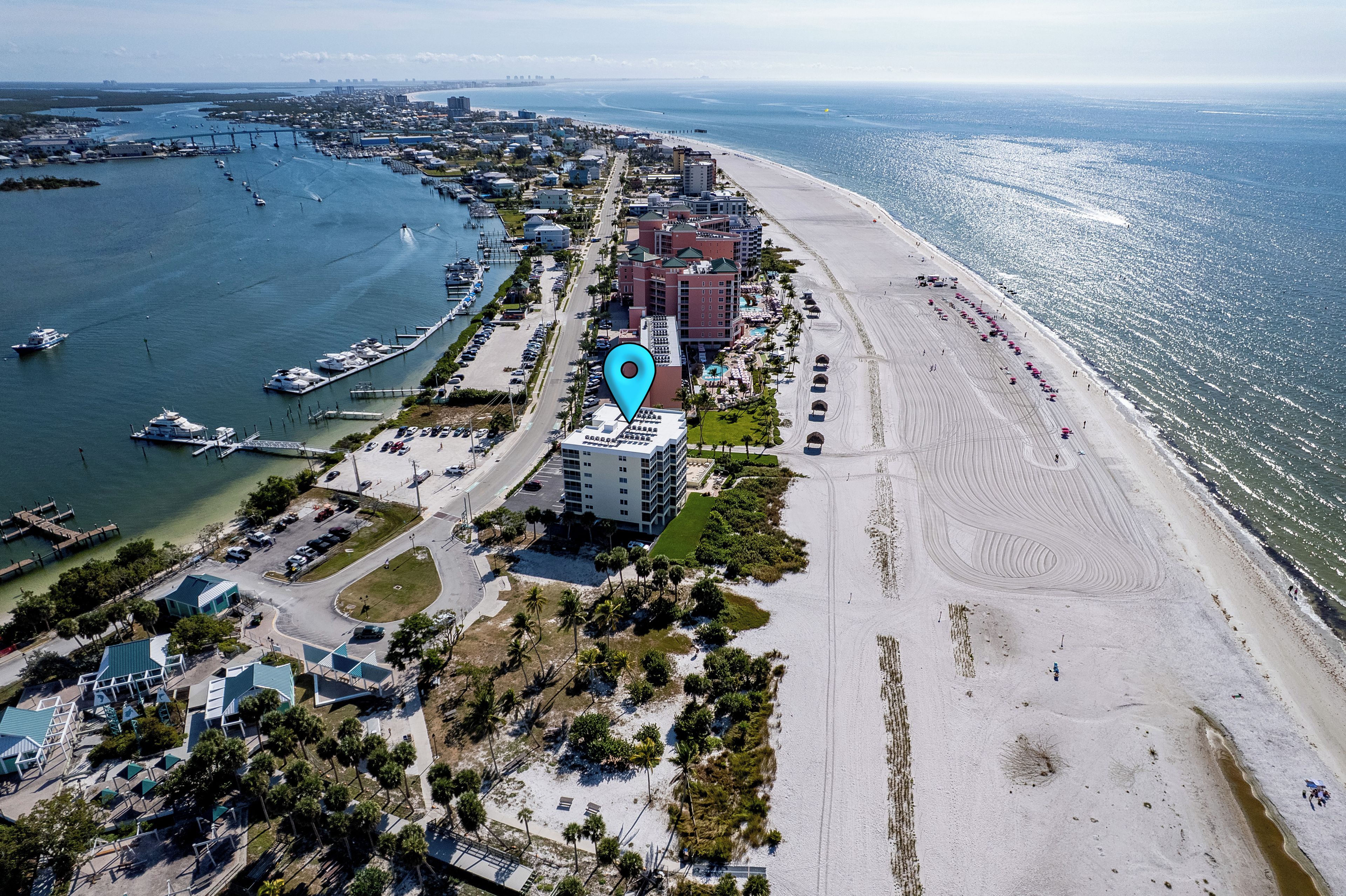 An aerial view of a coastal area with a marina, beachfront hotels, and a sandy beach.
