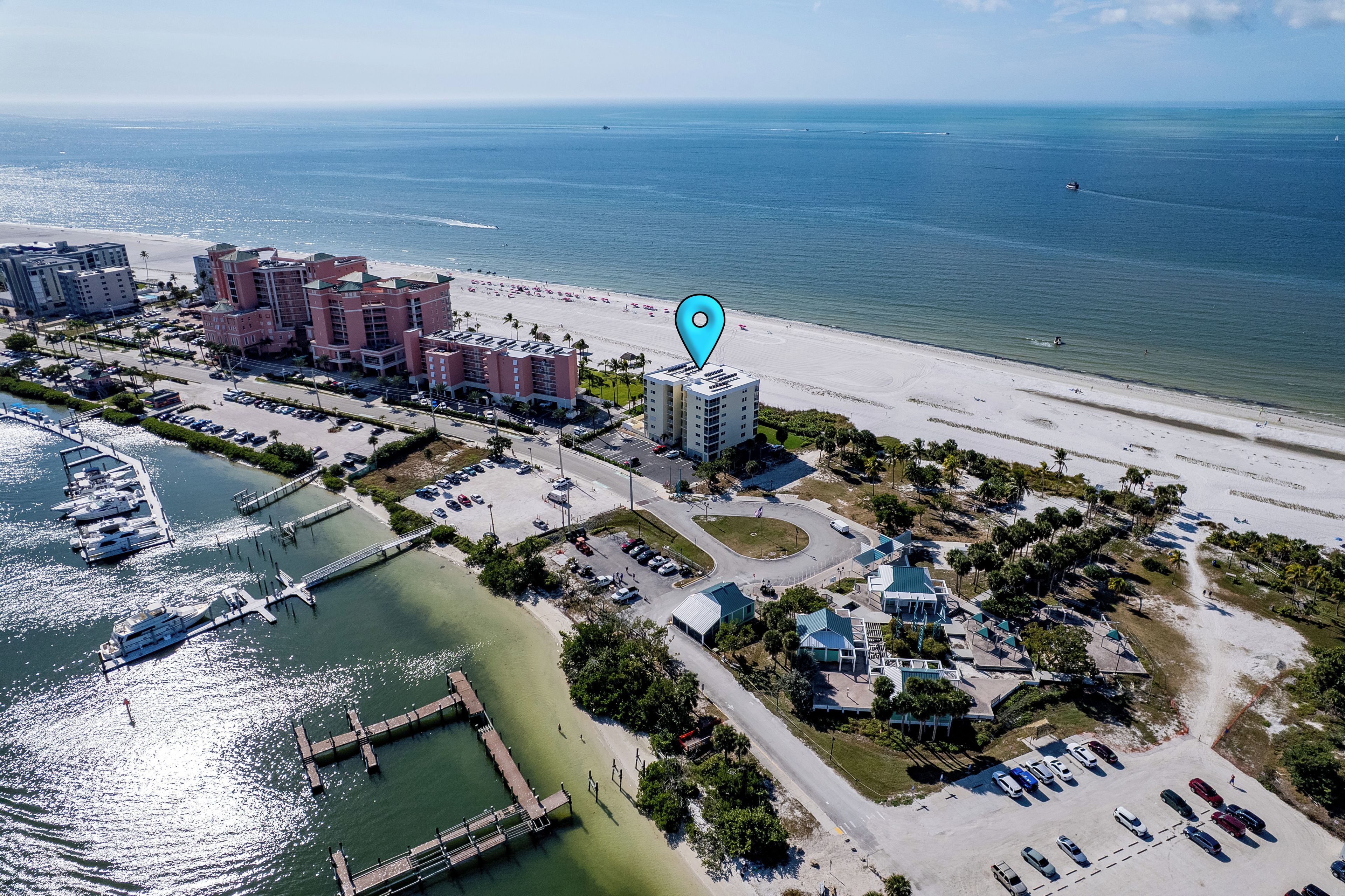 An aerial view of a coastal hotel area with a beach, parking, and a marina.