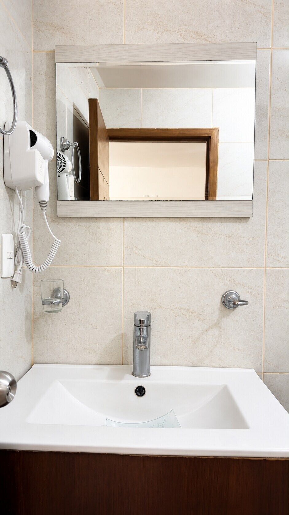 Casa de banho com lavatório branco, espelho, secador de cabelo e porta-toalhas.