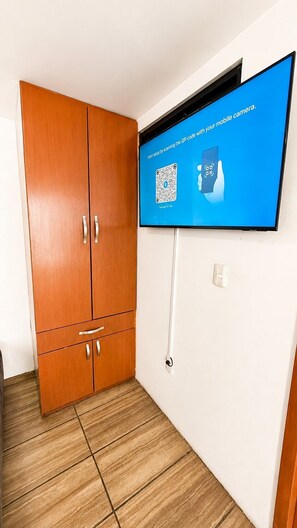 Ein Zimmer mit einem Holzkleiderschrank, einem flachbildschirmfernseher an der Wand und einem Fliesenboden.