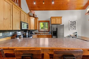 Eine Küche mit Holzausstattung, einem Edelstahlkühlschrank, einer Granitarbeitsplatte und einer Bar mit Hockern.