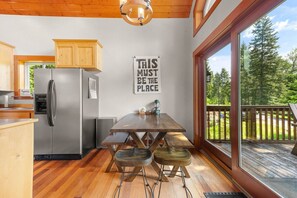 A modern kitchen with a stainless steel refrigerator, wooden cabinets, and a large window overlooking a deck. - River Rock Retreat | Hot Tub+A/C | Mt Rainier (Packwood)