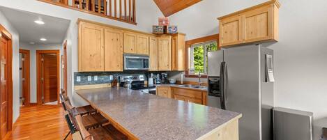 A spacious kitchen with wooden cabinets, a granite countertop, stainless steel appliances, and a dining area with benches.