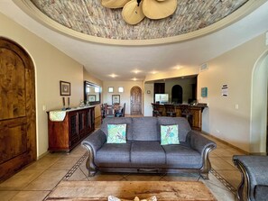 A spacious living room with a grey sofa, wooden cabinet, and a dining area in the background. - Bella Sirena B-202 (Puerto Peñasco)