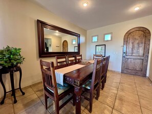 A dining area with a wooden table and chairs, a large mirror above the table, and a wooden door in the background. - Bella Sirena B-202 (Puerto Peñasco)