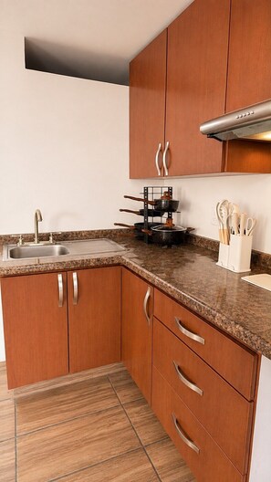 A kitchen with wooden cabinets, a granite countertop, a stainless steel sink, and a pot rack. - Bowra Suite Privada 4, Colonia Americana (Guadalajara)