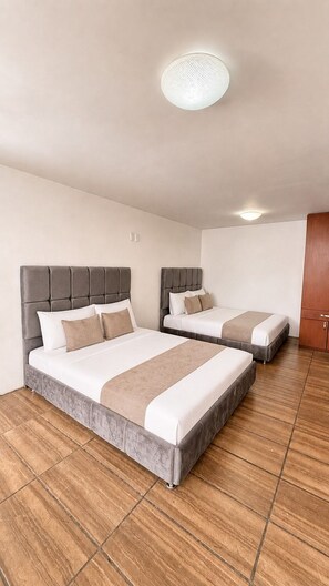 Ett hotellrum med två sängar, ett trägolv, en taklampa och en garderob i trä.