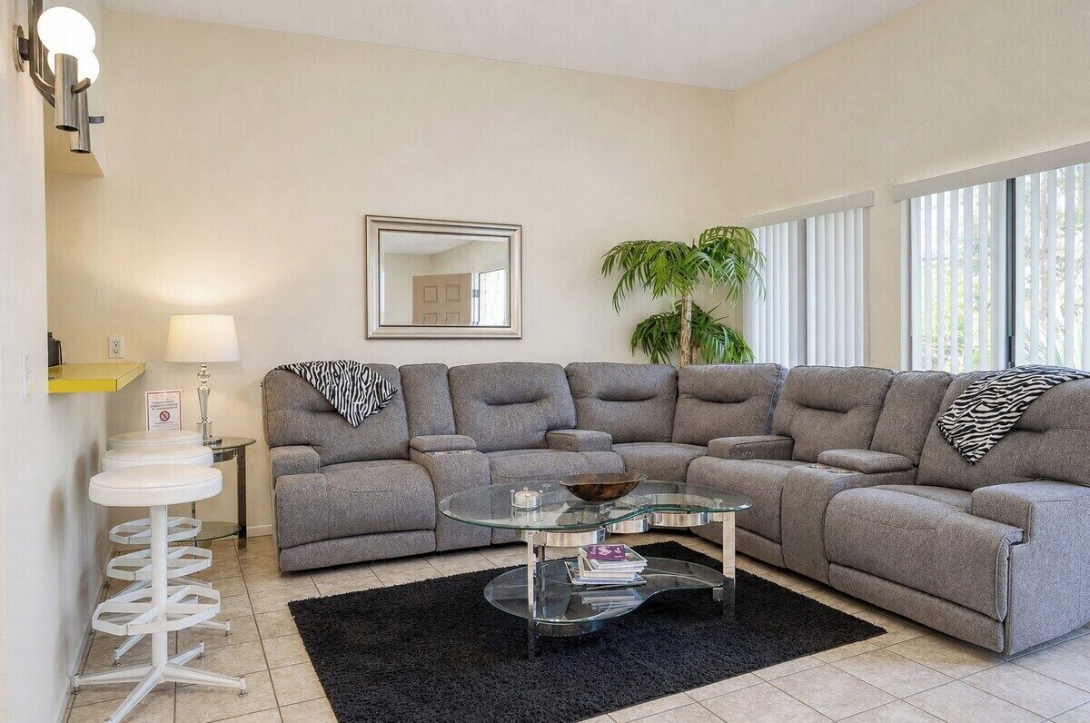 A modern living room with a sectional sofa, a glass coffee table, and a black rug.