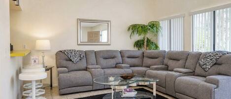 A modern living room with a sectional sofa, a glass coffee table, and a black rug.