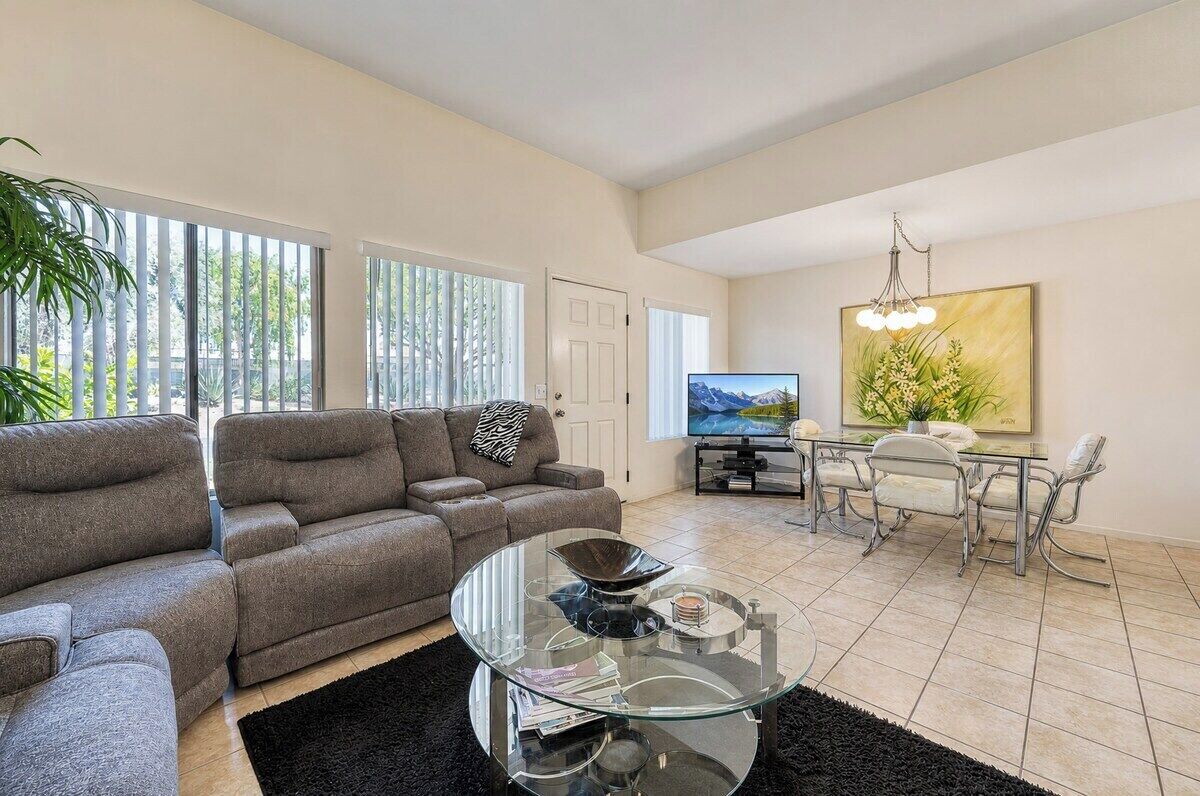 A living room with a sofa, a glass coffee table, a TV, and a dining area with chairs.