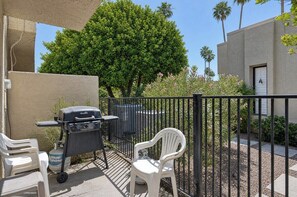 A patio with a barbecue grill, two white plastic chairs, and a large tree in the background. - Villa De Las Flores - South Palm Springs (Palm Springs)