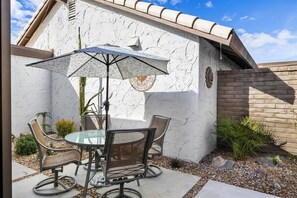 Un patio exterior con una mesa redonda y sillas, una sombrilla solar y una planta de cactus.