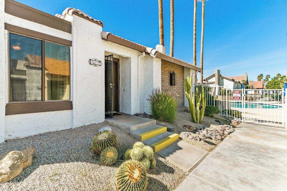 A residential property with a white exterior, a front door, a small porch, and a pool area with a fence.