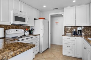 A kitchen with white cabinets, a white refrigerator, a microwave, a stove, and a granite countertop. - Canyon Sands Beauty (Palm Springs)