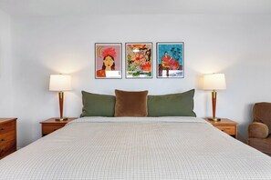 Ein Schlafzimmer mit einem Bett, zwei Nachttischen, einem Beistelltisch und drei gerahmten Kunstwerken an der Wand.