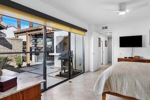 A modern bedroom with a bed, a TV, and a sliding glass door leading to a patio area. - Canyon Sands Beauty (Palm Springs)