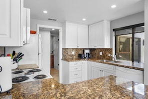 A modern kitchen with white cabinets, granite countertops, a built-in stove, and a window with a view. - Canyon Sands Beauty (Palm Springs)