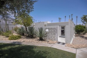 Un edificio moderno con facciata bianca, un ingresso carrabile e un giardino curato con diverse piante.